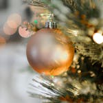 Close-up of a golden Christmas ornament hanging on a beautifully decorated tree with blurred festive lights.