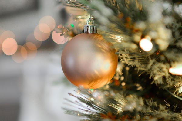 Close-up of a golden Christmas ornament hanging on a beautifully decorated tree with blurred festive lights.